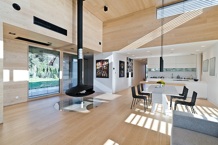 Single-storey house in Poland, clad almost entirely with cedar planks, has impressive double-height suspended fireplace in the open plan living room