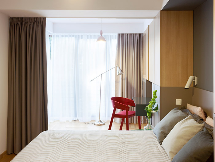 Modern bedroom design with small wood desk and red chair in a stylish, functional apartment in Bucharest by Rosu-Ciocodeica