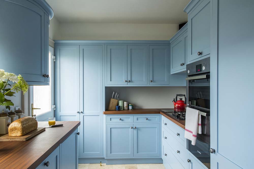 Traditional enclosed kitchen with light blue shaker cabinets, wooden countertops and white backsplash