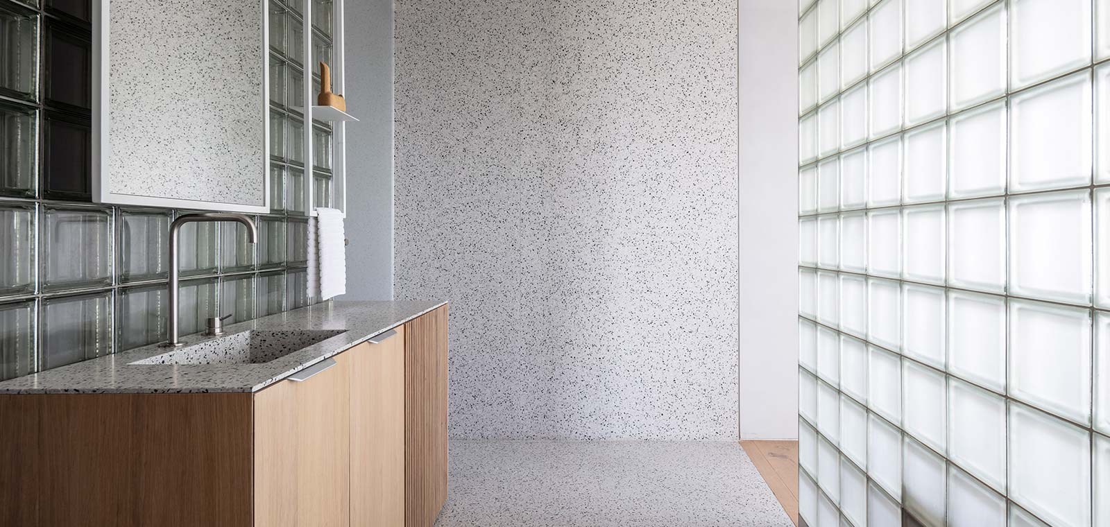 A glass block wall separates the sleeping area from the dressing area and bathroom in a bright duplex apartment located in Tel Aviv, Israel